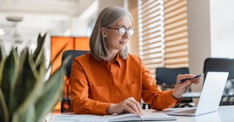 Older Executive Assistant sorting through meeting costs on her laptop