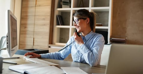 Businesswoman wearing glasses and with a ponytail on the phone and working on her laptop in the office