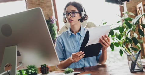Executive Assistant in her office working on her desktop, holding notepad in her hands, while listening to a podcast