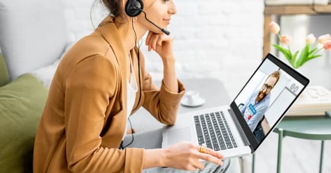 Female assistant working from home wearing headphones as she meets with a colleague virtually